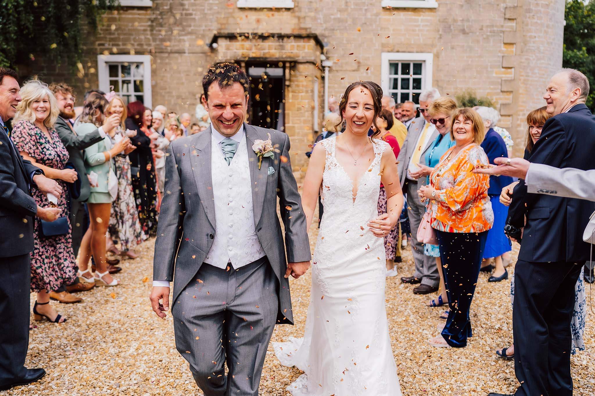 bride and groom walk through a cloud of confetti during their wedding day at Cockliffe House in Nottinghamshire
