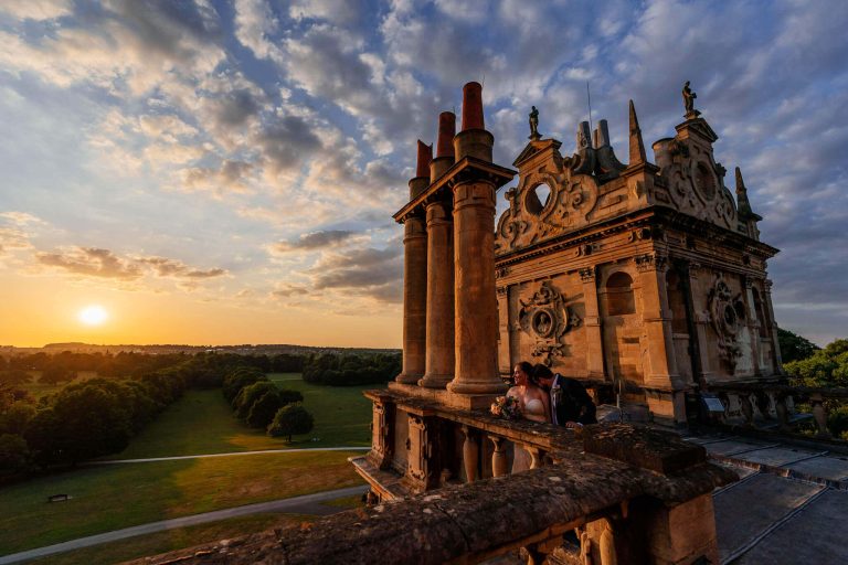 Bride and groom cuddle and look out towards the beautiful sunset on top of Wollaton Hall in Nottingham during a quiet time at their wedding
