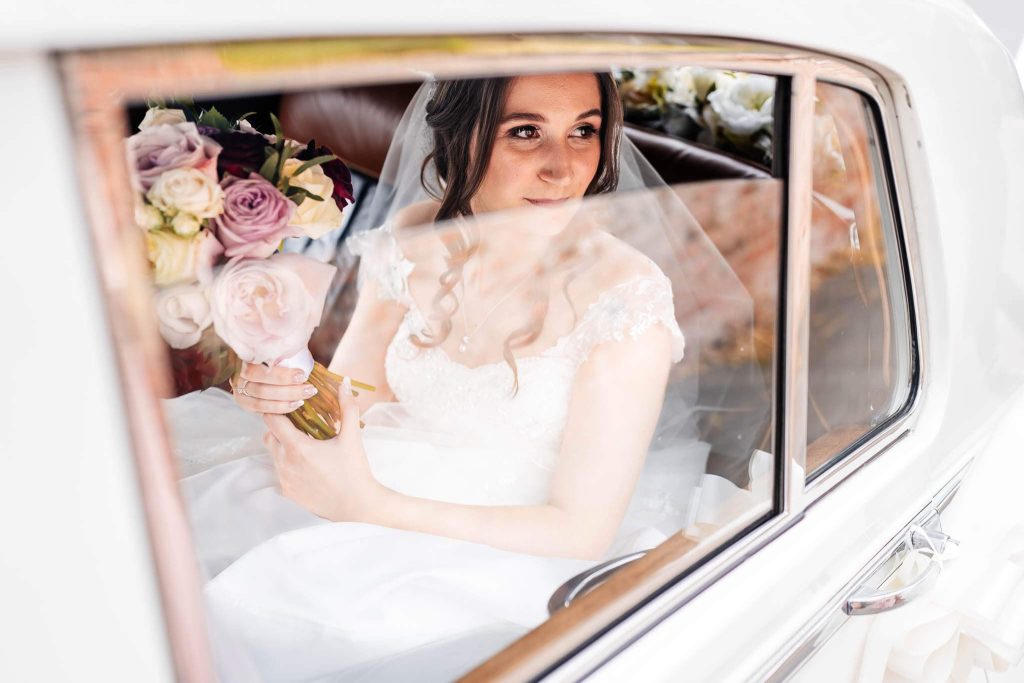Bride looks out of a slightly opened window of the wedding car as she waits for the rest of her guests to go in the church