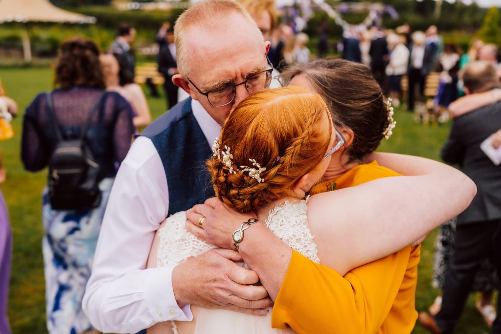 Bride has a big hug from her parents after her wedding ceremony at Bridge House Barns