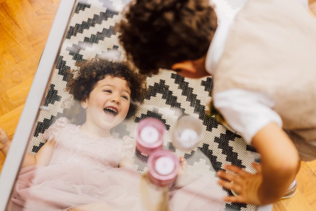flower girl laughs at the page boy pulling a funny face at her through a glass table at Thornbridge Estate in the Peak District