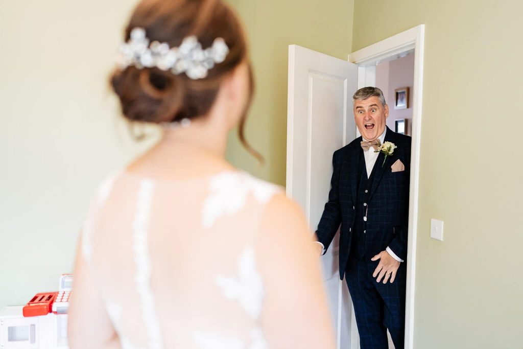 Father of the bride looks very surprised seeing his daughter the bride in her dress for the first time