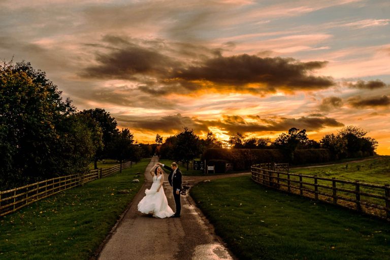 Bride and groom dance with the sun setting over the top of Mythe Barn in the background
