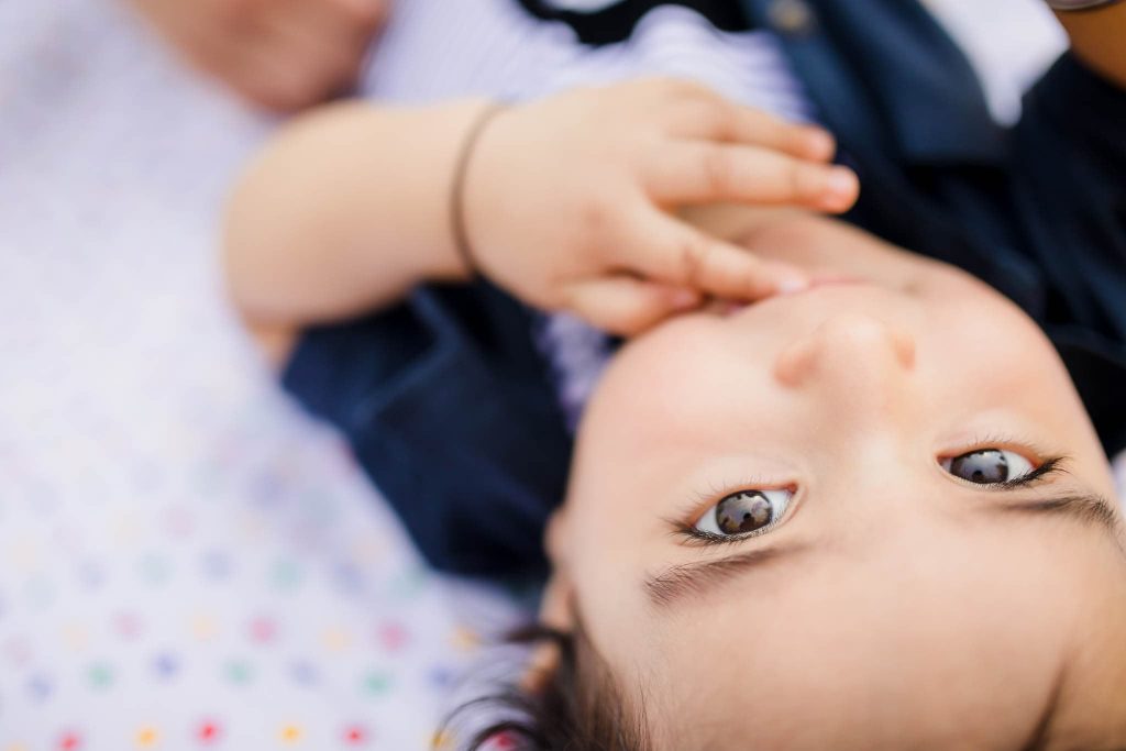 A baby, captured by a Leicester family photographer, lies on a patterned blanket, gazing upwards. Their tiny hand is near their mouth, and they don a dark outfit. The image offers a close-up from an overhead angle, perfectly capturing this tender moment.